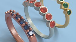 Three rings with different designs and gemstones are displayed on a light blue background. The first ring is rose gold with blue stones and small bead accents. The second ring is silver with orange stones, each set in circular bezels. The third ring is gold
