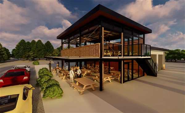 A modern two-story building with a spacious outdoor patio and seating area. The ground floor features several wooden picnic tables, some occupied by people, while a staircase leads to an upper level with additional seating and glass railings. Several cars are parked nearby,