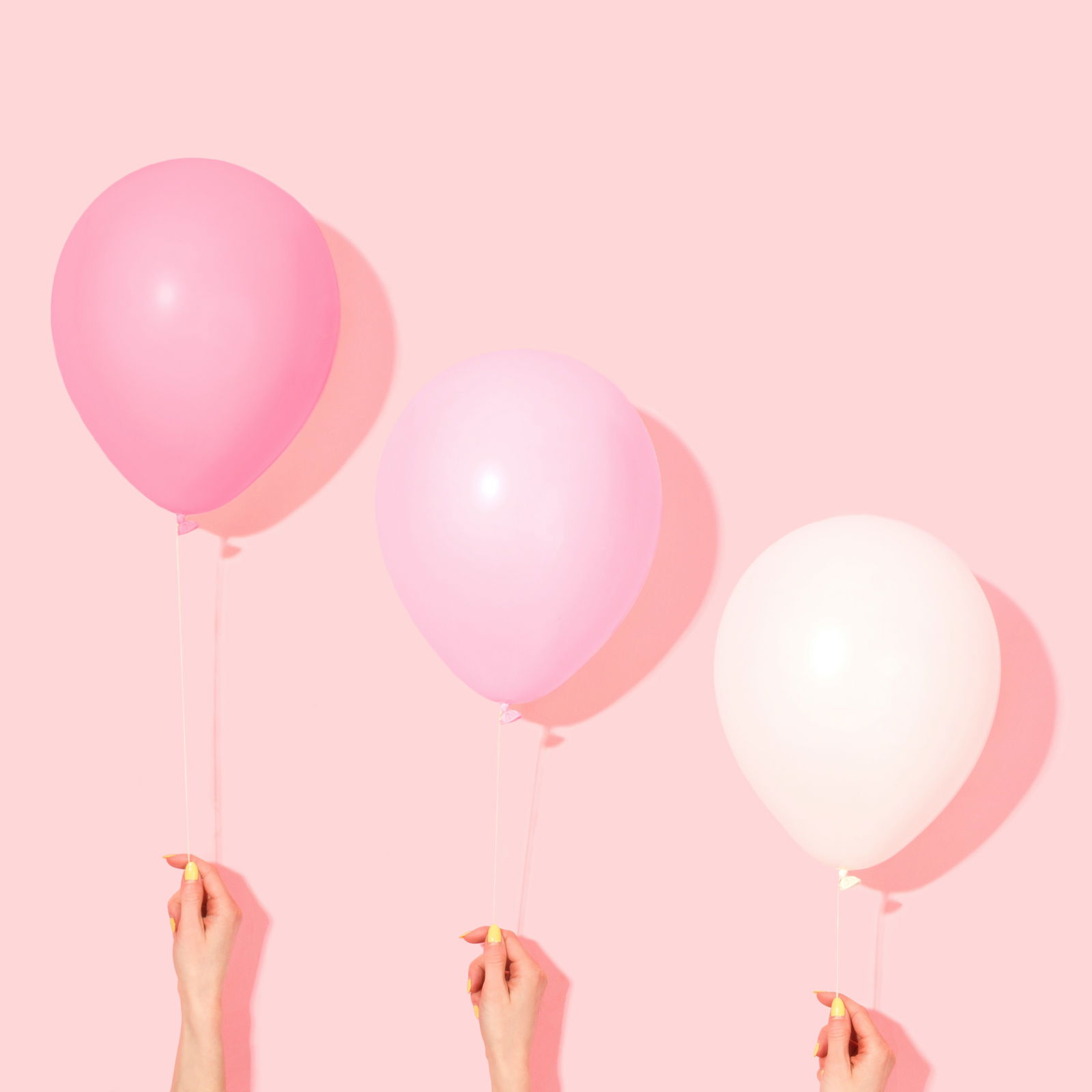 Three hands, each holding a string attached to a balloon, are shown against a pink background. The three balloons from left to right are in shades of pink and white.